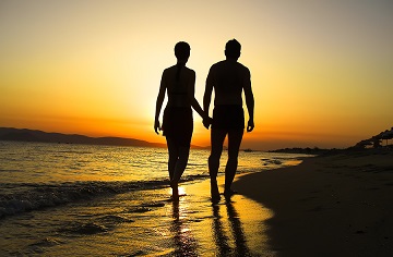 夕日のビーチを歩くカップル